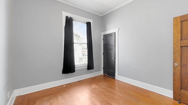 empty room featuring visible vents, crown molding, light wood-type flooring, and baseboards