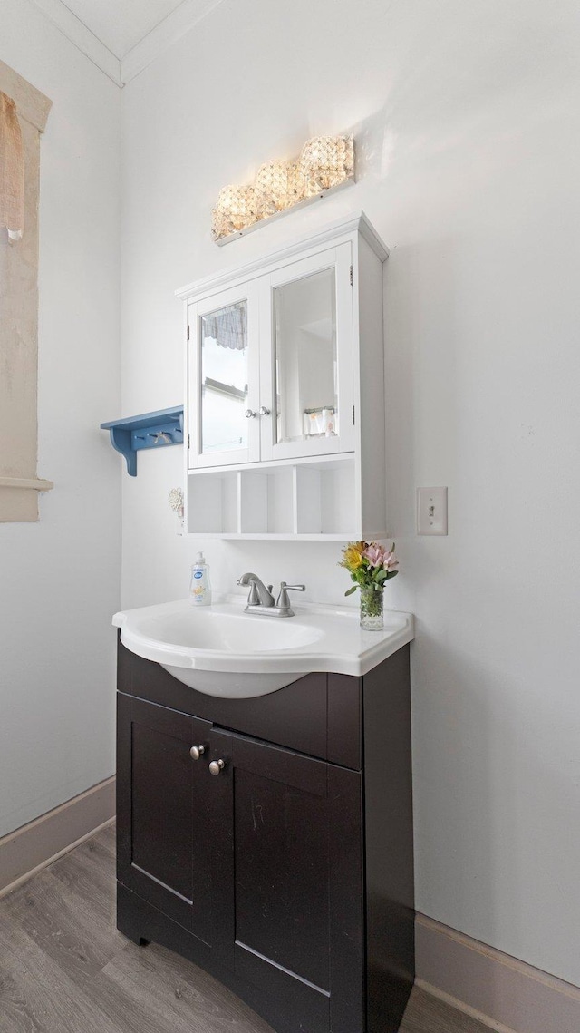 bathroom with baseboards, wood finished floors, vanity, and ornamental molding