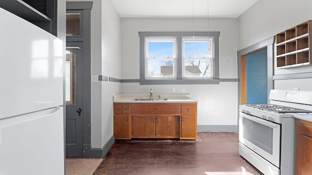 kitchen with brown cabinets, dark wood-type flooring, a sink, white appliances, and baseboards