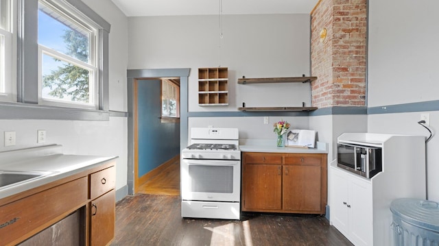 kitchen featuring light countertops, gas range gas stove, brown cabinetry, and dark wood-style flooring