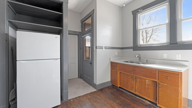 kitchen with freestanding refrigerator, a sink, dark wood-type flooring, light countertops, and brown cabinets