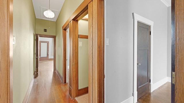 hall featuring light wood-style flooring, attic access, and baseboards