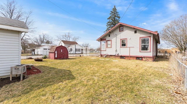 rear view of property featuring an outbuilding, a storage shed, a lawn, and fence