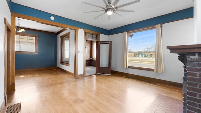 unfurnished living room featuring baseboards, visible vents, light wood-style flooring, a fireplace, and ceiling fan