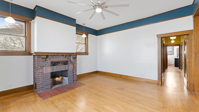 unfurnished living room featuring a brick fireplace, wood finished floors, baseboards, and ceiling fan