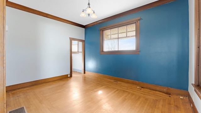 spare room featuring baseboards, visible vents, ornamental molding, wood-type flooring, and a chandelier