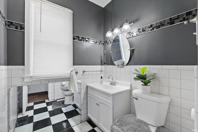 bathroom with a wainscoted wall, toilet, vanity, tile patterned floors, and tile walls