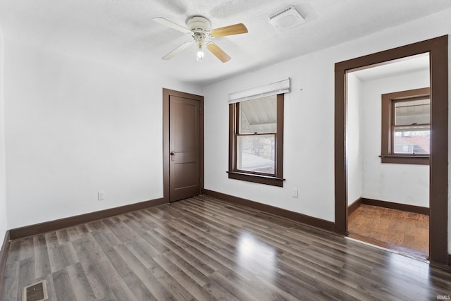 unfurnished room with baseboards, visible vents, dark wood-style flooring, and ceiling fan