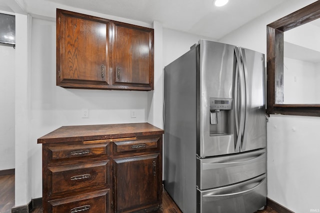 kitchen with dark countertops, dark brown cabinetry, stainless steel fridge, and baseboards