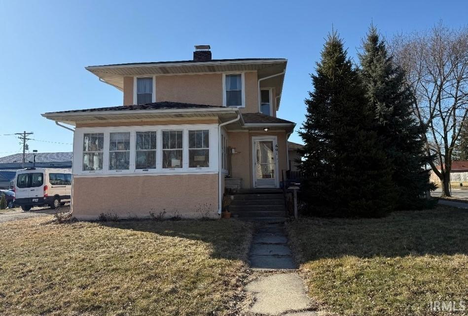 view of front of home with a front yard, a chimney, and stucco siding