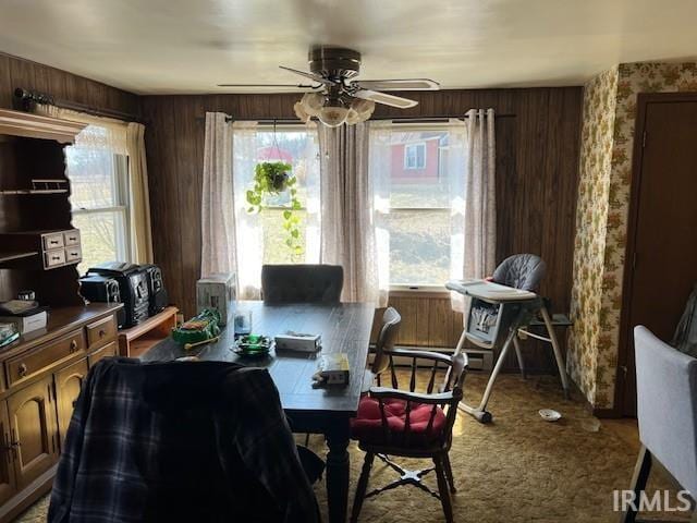 carpeted dining room with wooden walls and a ceiling fan