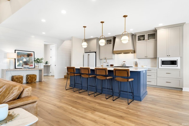 kitchen with premium range hood, light wood-type flooring, a center island with sink, open floor plan, and white appliances