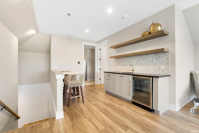 bar with beverage cooler, light wood finished floors, wet bar, and a sink