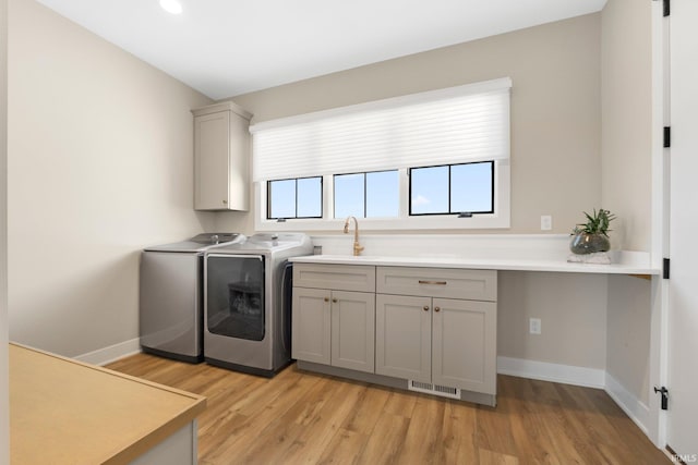 washroom with washing machine and clothes dryer, visible vents, light wood-style floors, cabinet space, and a sink