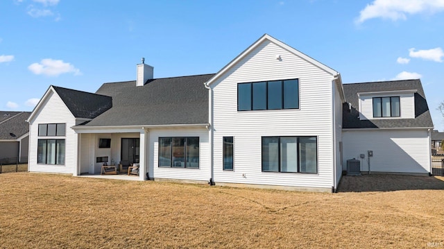 rear view of house featuring a shingled roof, central AC unit, a chimney, a yard, and a patio