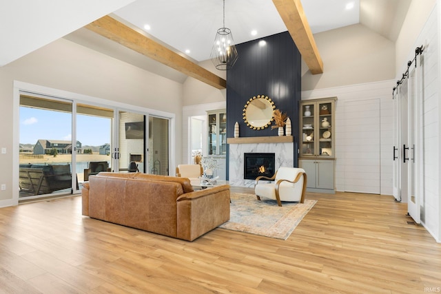 living room with light wood finished floors, a barn door, a fireplace, an inviting chandelier, and high vaulted ceiling