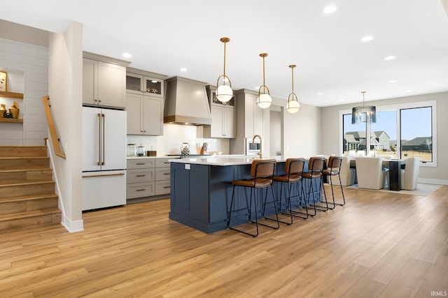 kitchen with high end fridge, gray cabinetry, a breakfast bar, wall chimney exhaust hood, and decorative backsplash