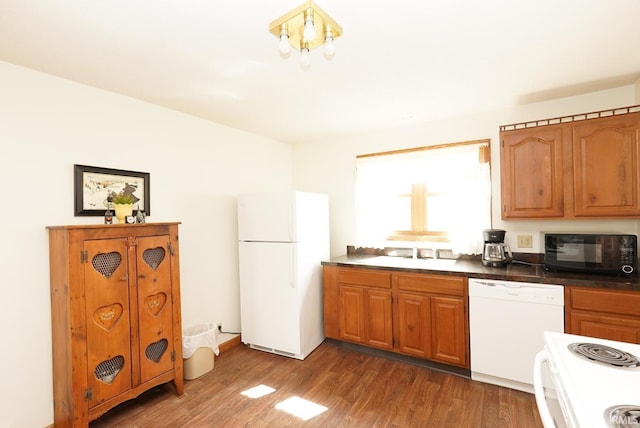 kitchen with brown cabinets, a sink, dark countertops, wood finished floors, and white appliances