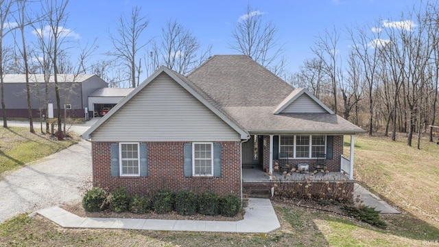 view of front facade with brick siding, covered porch, a front lawn, and a shingled roof