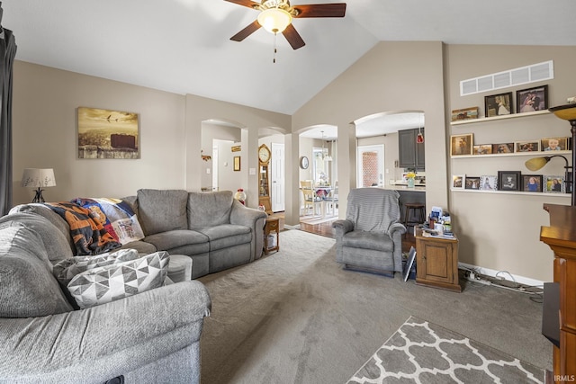 carpeted living room with visible vents, vaulted ceiling, arched walkways, a ceiling fan, and ornate columns