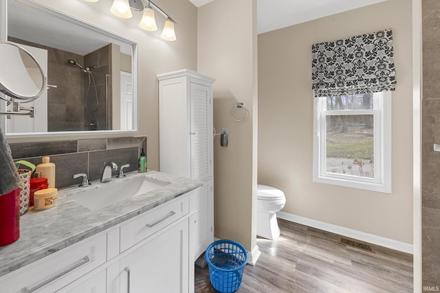 full bathroom featuring vanity, wood finished floors, baseboards, visible vents, and tiled shower