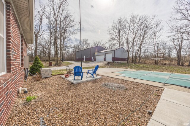 view of yard featuring an outbuilding, a patio area, a detached garage, and a covered pool