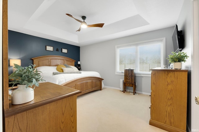 bedroom with light colored carpet, a raised ceiling, baseboards, and ceiling fan