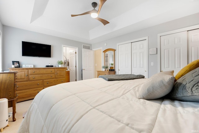 bedroom featuring visible vents, two closets, a ceiling fan, a raised ceiling, and light colored carpet