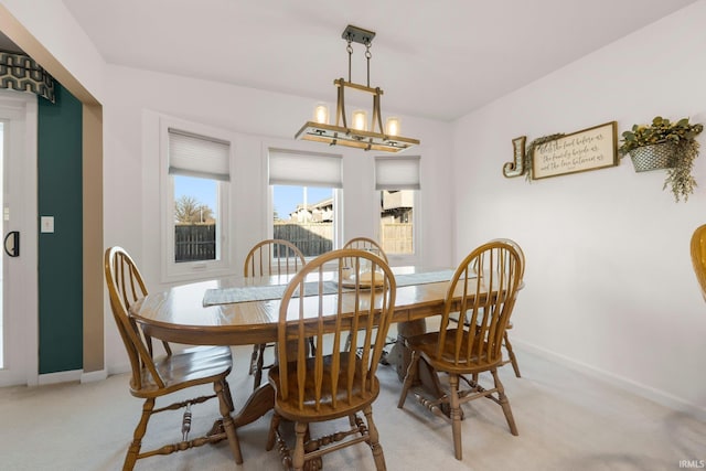 dining area featuring an inviting chandelier, light colored carpet, and baseboards