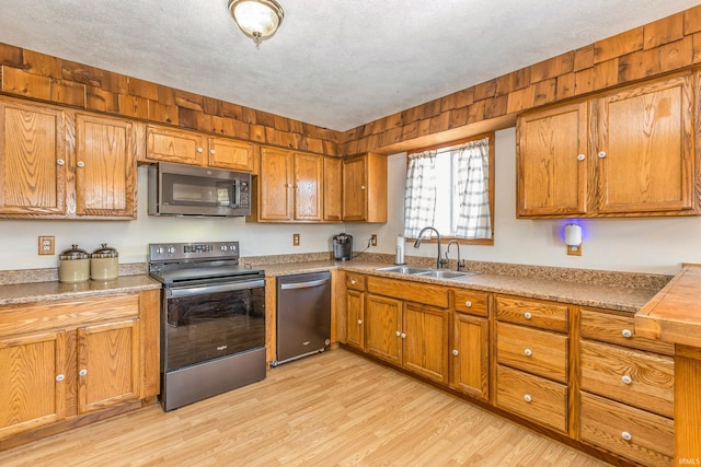 kitchen with light wood-style flooring, a sink, a textured ceiling, stainless steel appliances, and brown cabinetry