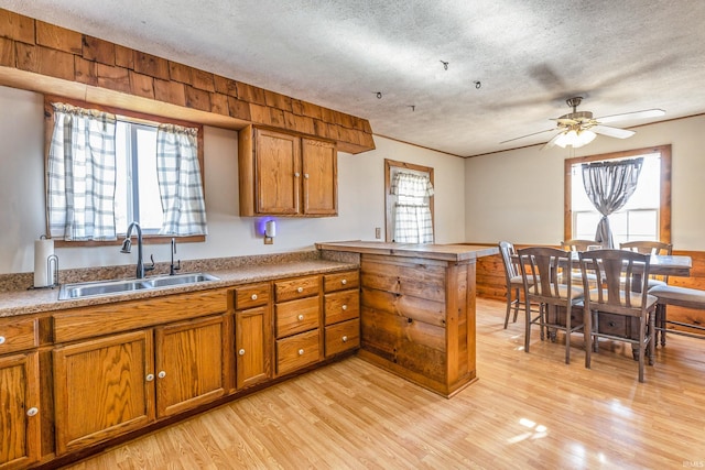 kitchen with brown cabinets, a peninsula, light wood-style flooring, a textured ceiling, and a sink