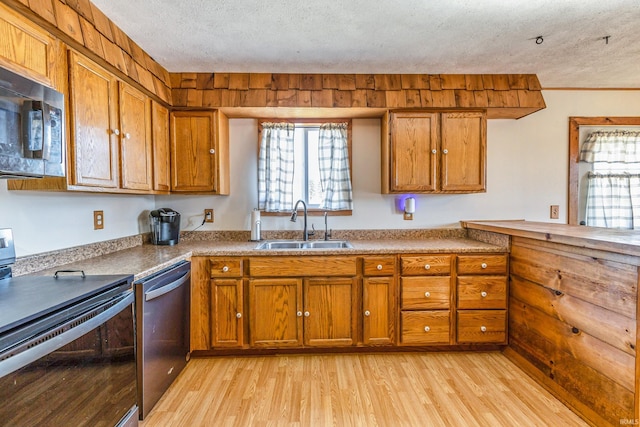 kitchen featuring light wood-type flooring, brown cabinets, a sink, a textured ceiling, and stainless steel appliances