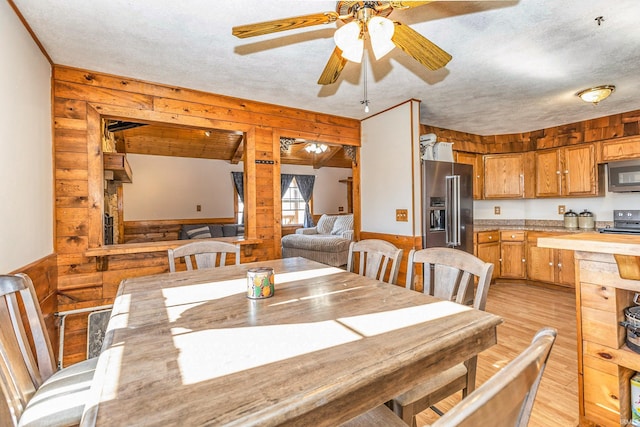 dining space featuring a textured ceiling, light wood-style floors, a wainscoted wall, and ceiling fan