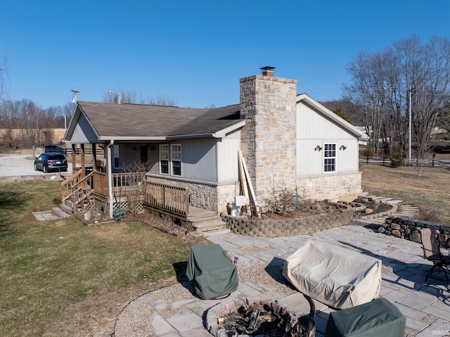 rear view of property with stone siding, a patio, a yard, roof with shingles, and a chimney