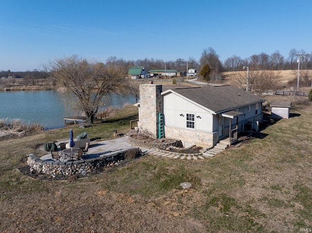 view of side of property with a water view, roof with shingles, a chimney, a yard, and a patio