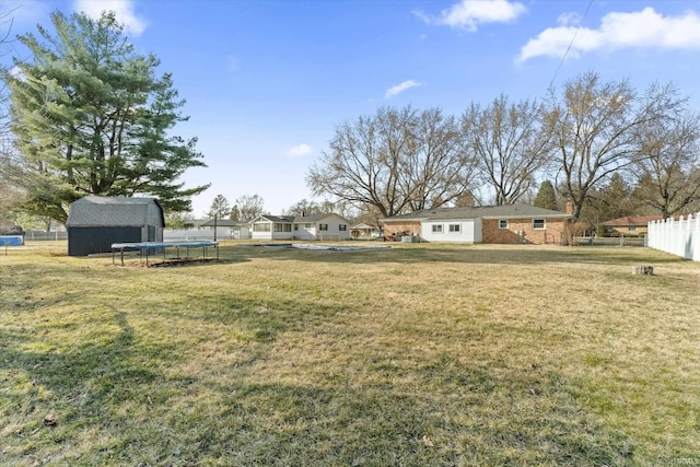 view of yard with a storage shed, an outdoor structure, a trampoline, and fence