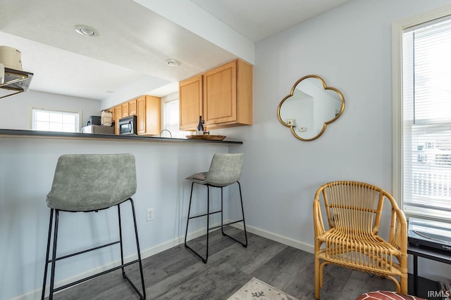 kitchen with a breakfast bar area, light brown cabinets, baseboards, dark wood-style flooring, and black microwave