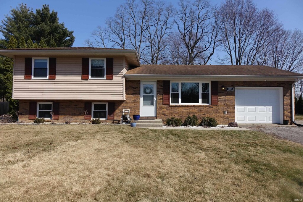 tri-level home featuring a garage, brick siding, a front yard, and aphalt driveway