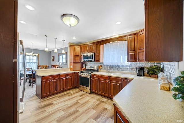 kitchen with a sink, backsplash, stainless steel appliances, a peninsula, and light countertops