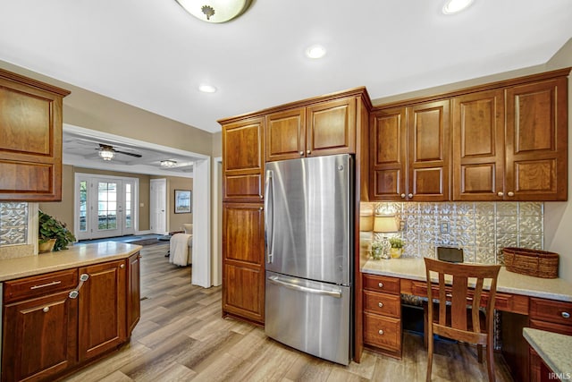 kitchen featuring light wood-style flooring, freestanding refrigerator, ceiling fan, decorative backsplash, and built in desk