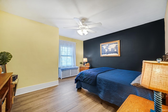 bedroom with ceiling fan, baseboards, wood finished floors, and an accent wall