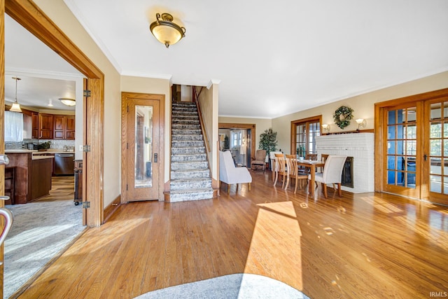 living room with ornamental molding, stairway, french doors, light wood-style floors, and baseboards