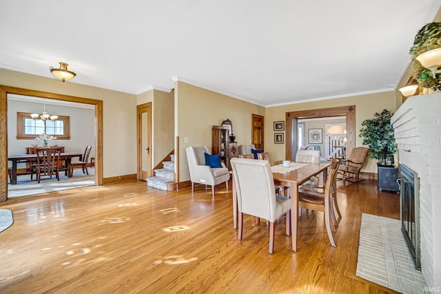 dining area featuring a chandelier, a brick fireplace, stairs, and light wood-style floors