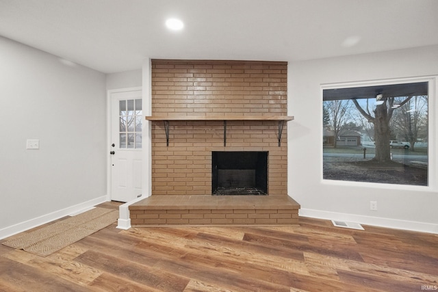 unfurnished living room featuring visible vents, wood finished floors, recessed lighting, baseboards, and a brick fireplace