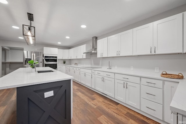 kitchen with wood finished floors, white cabinetry, appliances with stainless steel finishes, wall chimney exhaust hood, and hanging light fixtures