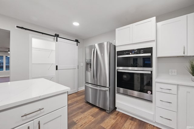 kitchen with light stone countertops, dark wood finished floors, a barn door, appliances with stainless steel finishes, and white cabinets