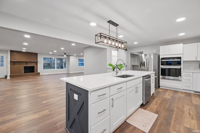 kitchen featuring wood finished floors, a kitchen island with sink, stainless steel appliances, a sink, and white cabinetry