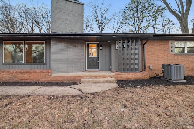 view of front facade with cooling unit, brick siding, and a chimney