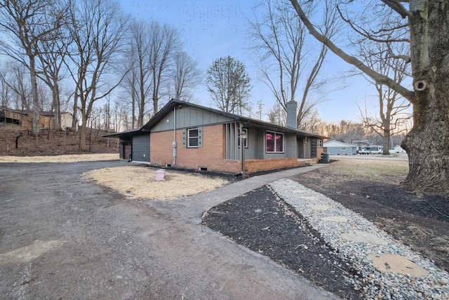 view of front of home featuring central AC unit, brick siding, a chimney, and driveway