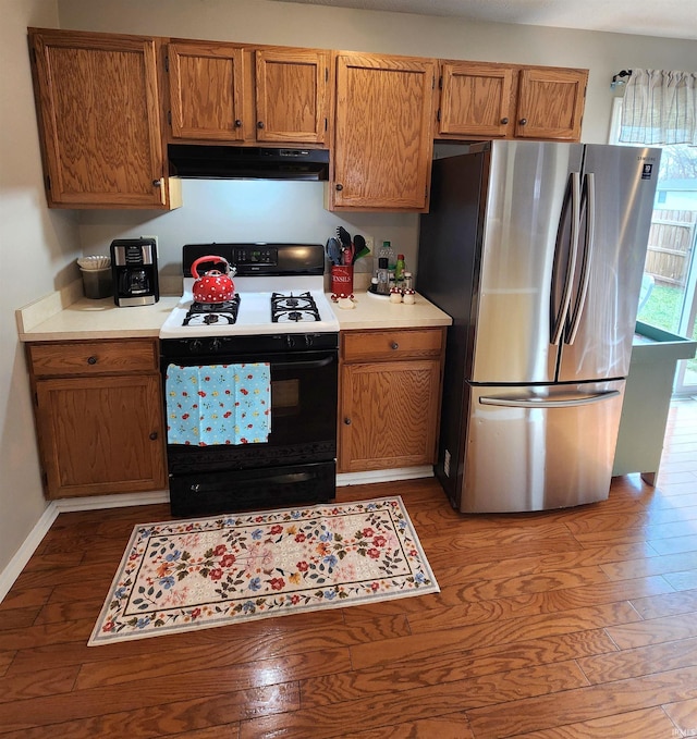 kitchen with wood finished floors, gas stove, freestanding refrigerator, light countertops, and under cabinet range hood